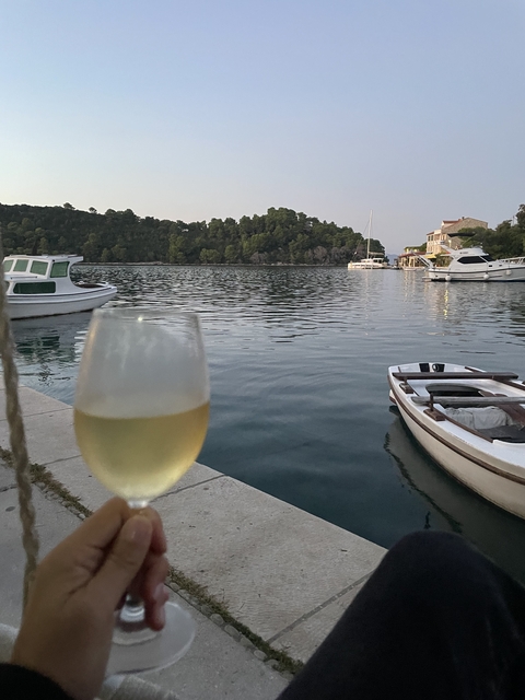       Wine glass by the waterside with boats in the background.
  