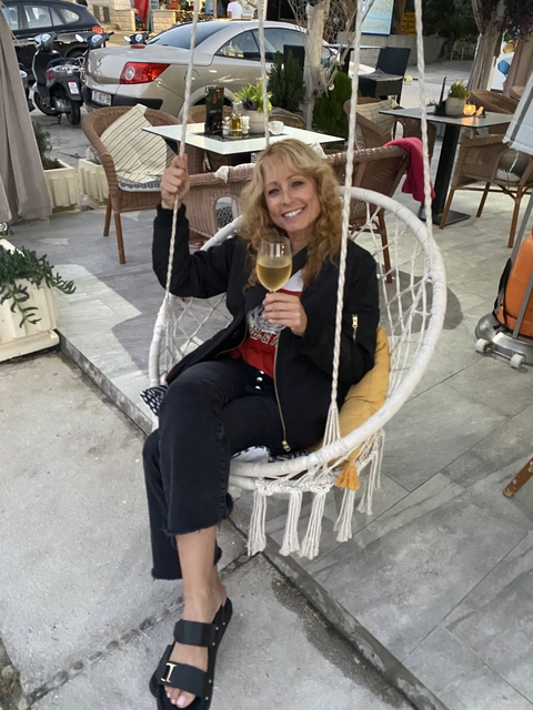       A woman sitting in a swing chair with a drink.
  