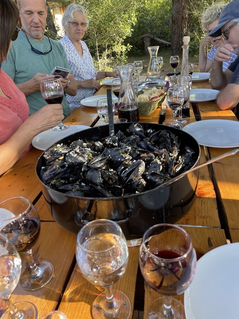       Large pot of mussels on a wooden table with wine glasses.
  