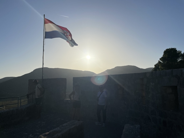       Silhouette of people with a Croatian flag against a sunset.
  