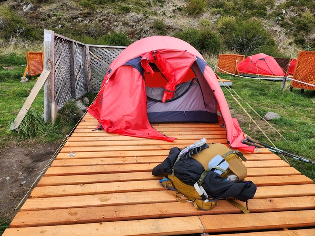Red tent pitched on a wooden platform in a grassy area.