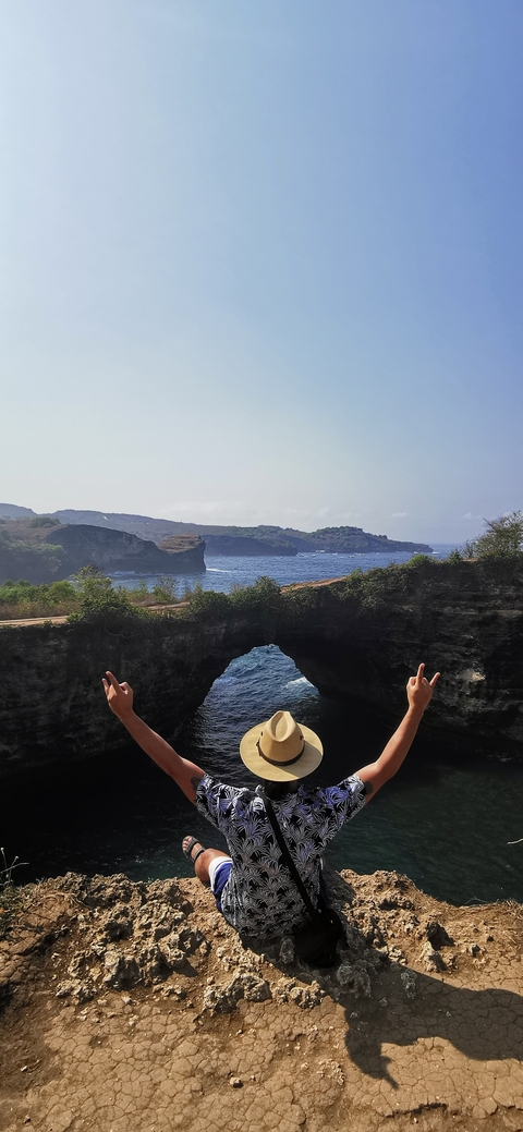       Hands showing peace signs over a natural arch with ocean background.
  