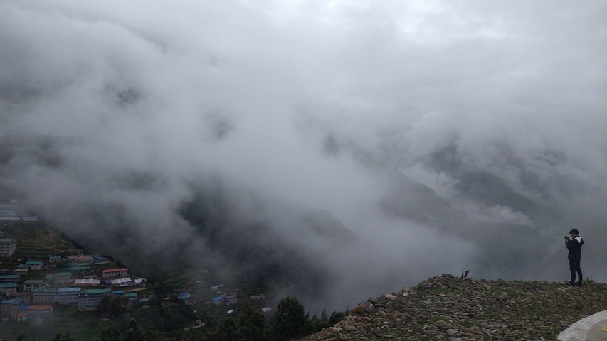 Person standing with a camera phone in a foggy mountain setting.