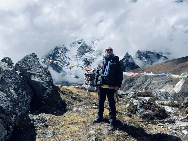       Person standing in front of mountains with prayer flags.
  