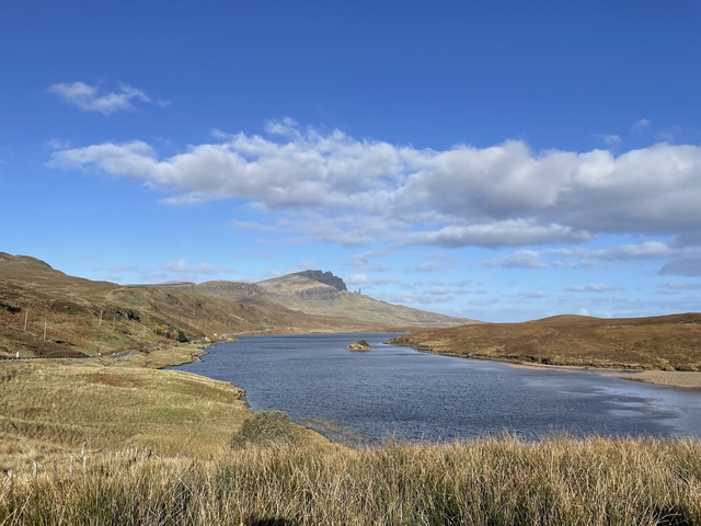       Loch with mountainous backdrop and cloudy sky.
  