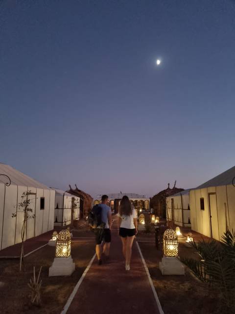       Two people walking on a lit path at dusk, under a full moon.
  