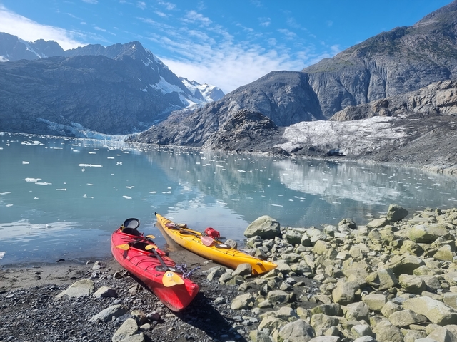       Kayaks on a rocky shore with glaciers in the background.
  