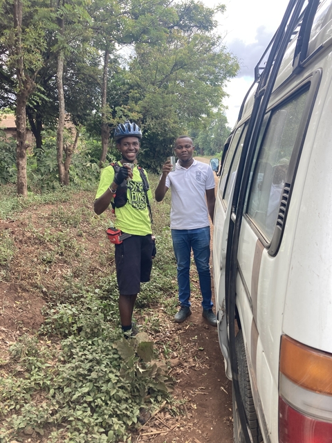      Two people standing next to a van among greenery.
  