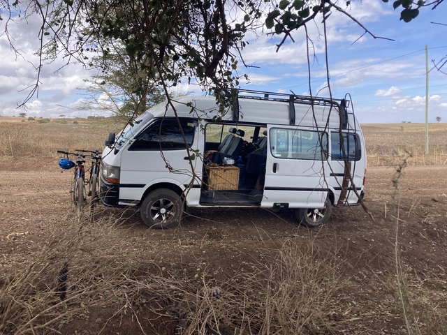       White van parked on a dirt road with bicycles nearby.
  