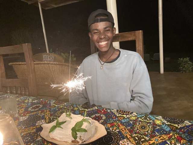       Person smiling at a table with a sparkler, outdoors at night.
  