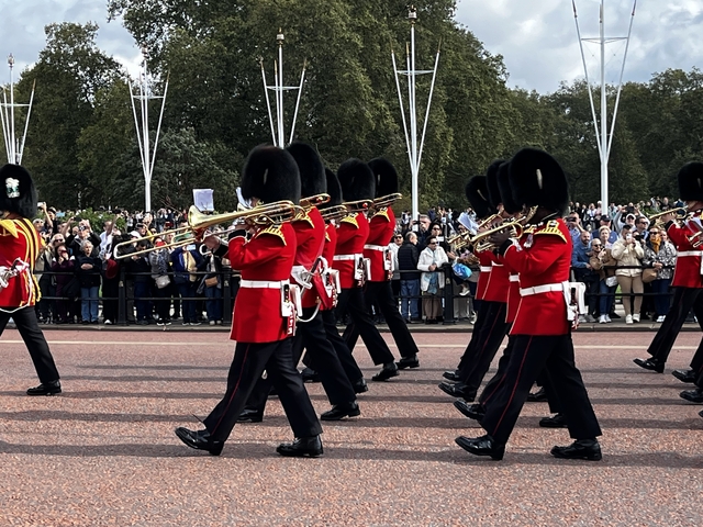       Marching band in red uniforms parading with a crowd watching.
  