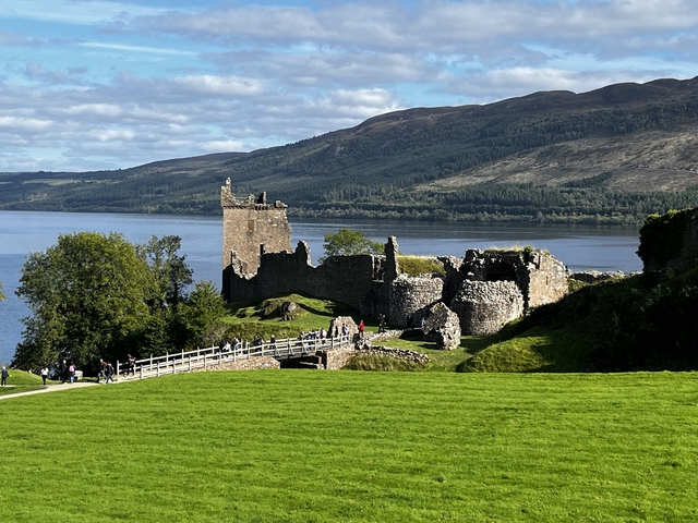       Ruins of a historic castle by a loch with mountains in the background.
  