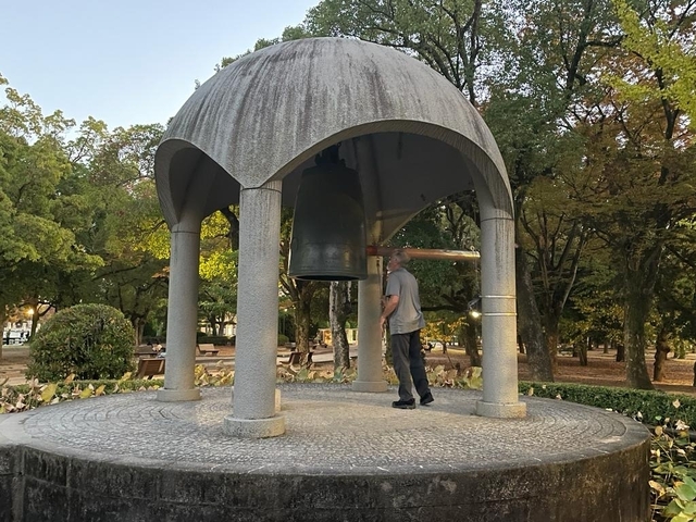       Person standing by a large bell structure in a park.
  