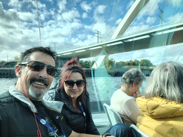       Couple on a boat trip with a bridge and river view.
  