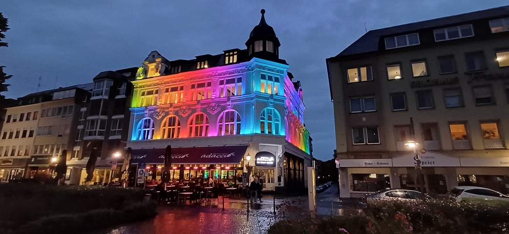       Buildings illuminated in rainbow colors in a town square at dusk.
  