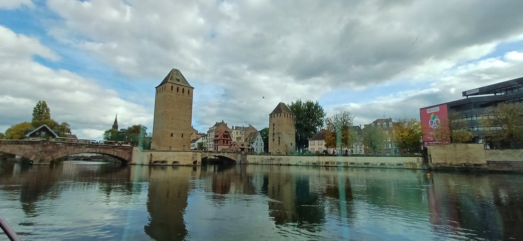       Historic buildings by a river under a cloudy sky.
  