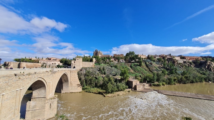 River with arched stone bridge and historic town on a hill.