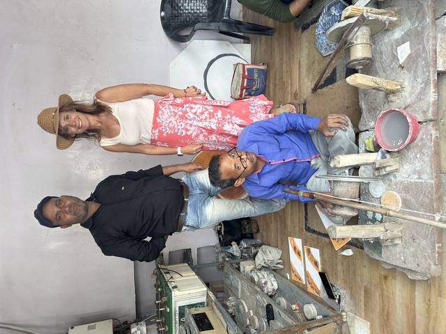 Three people inside a workshop, including a woman in a summer dress and men sitting on the floor.