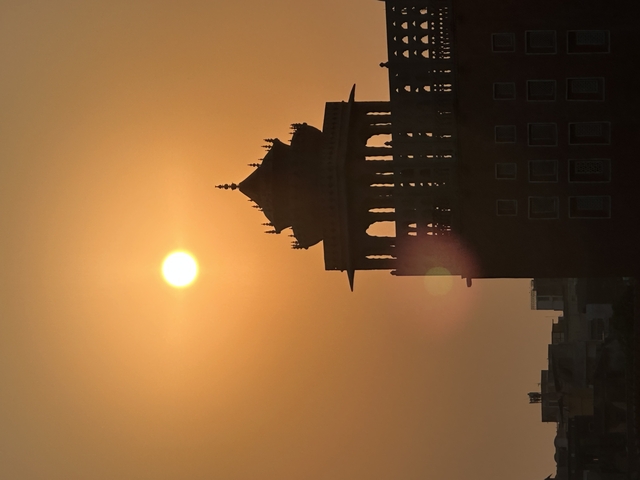 Silhouette of a building with a domed roof against a setting sun.
