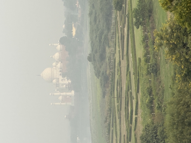 Distant view of the Taj Mahal with greenery in the foreground under a hazy sky.