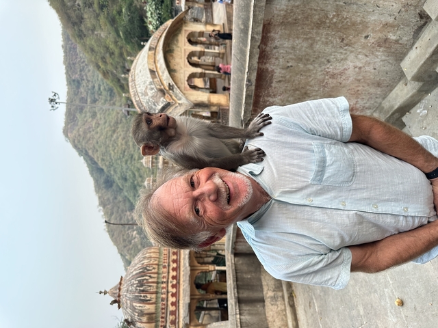Man smiling with a monkey on his shoulder in an outdoor setting.