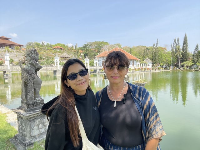 Two people posing by a serene pond with traditional Balinese architecture.