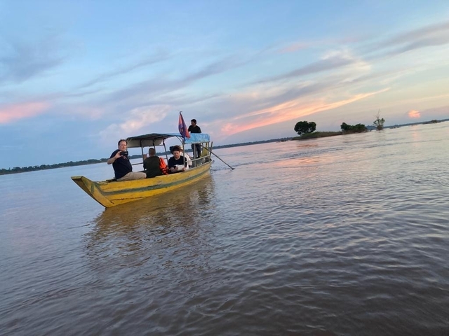       People in a small boat on a river during sunset.
  