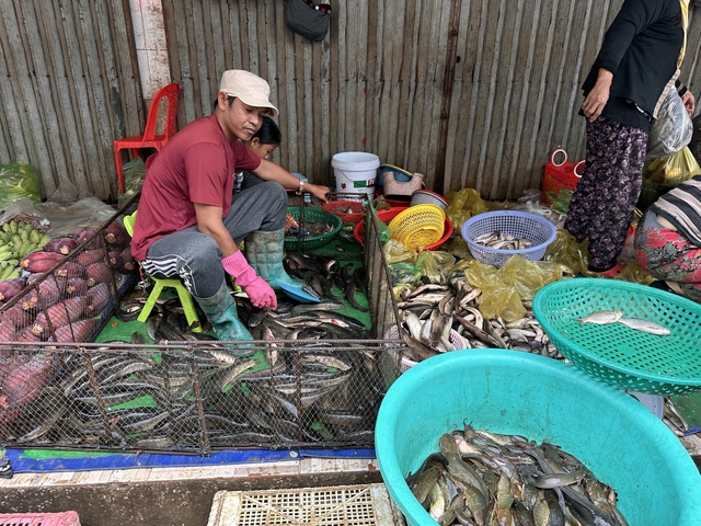       People selling fish at a market, surrounded by containers.
  