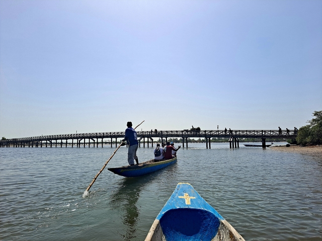       People paddling a boat on a calm river with a bridge in the background.
  