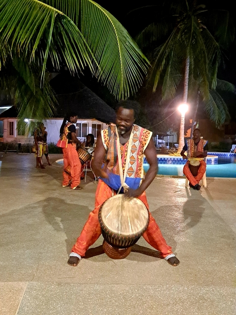       Performers in traditional dress playing drums by a pool at night.
  