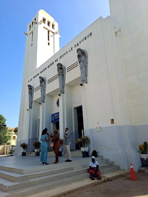       White church with statues and people entering.
  