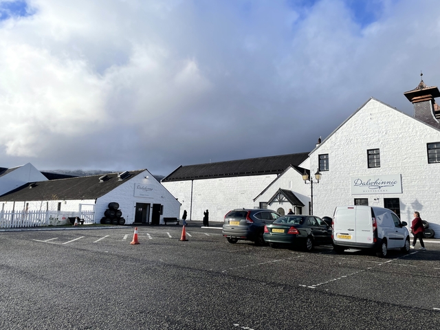       Dalwhinnie Distillery buildings with parked cars and a cloudy sky.
  