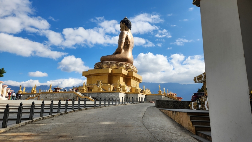       Large Buddha statue with blue sky and clouds.
  