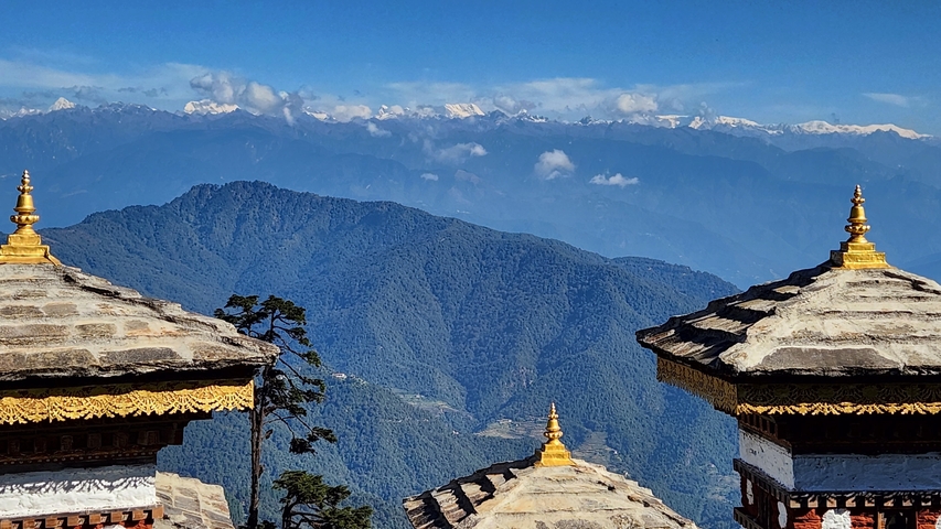       View over a mountain range with stupas in the foreground.
  
