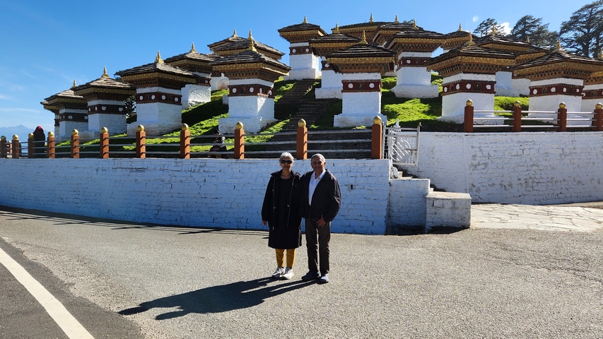       Two people standing in front of multiple stupas on the road.
  