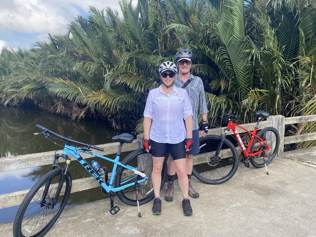       Two people standing with bicycles on a bridge surrounded by lush greenery.
  
