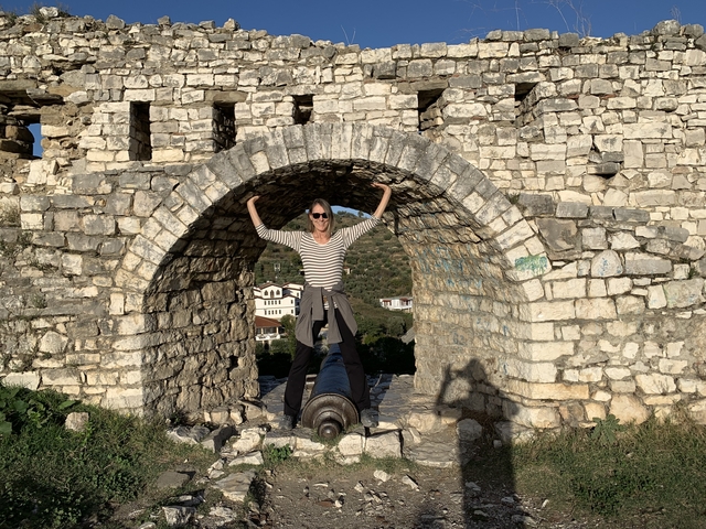       Person posing with arms up in a stone archway of a historic structure.
  
