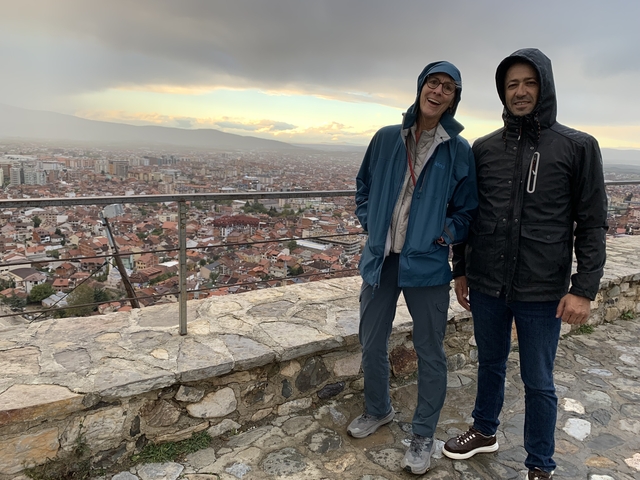       Two people posing on a terrace overlooking a city.
  