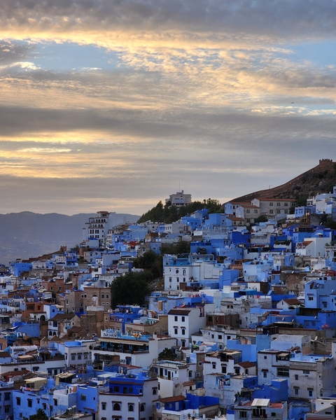 Panoramic view of a city with blue-painted buildings under a cloudy sky.