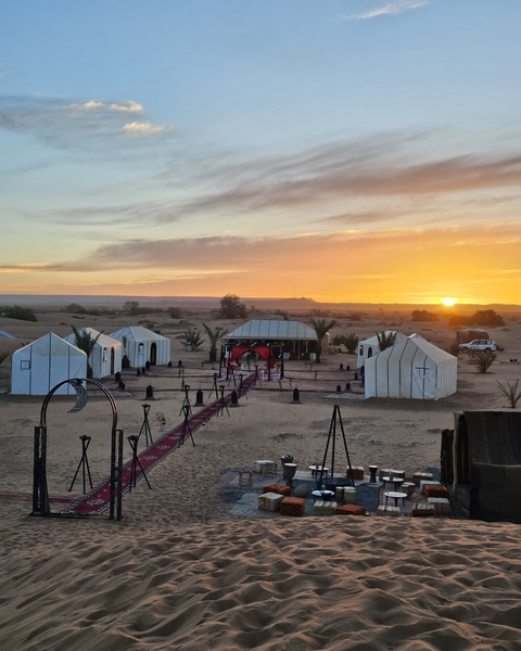Desert camp with tents and decorative pathway at sunset.