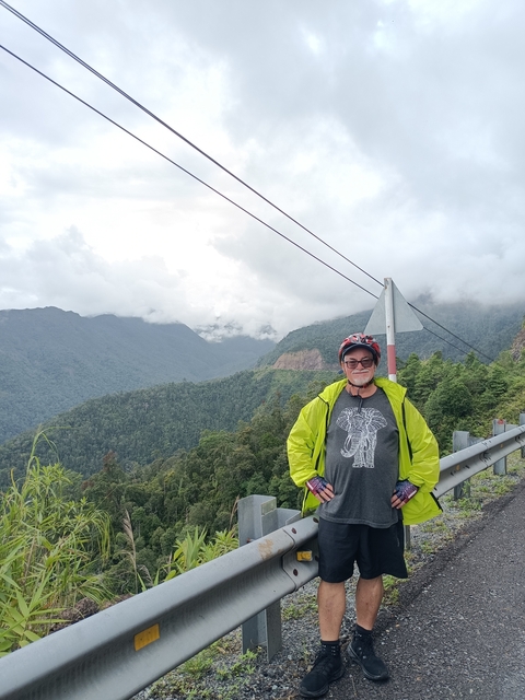       Cyclist in a green jacket posing with a mountain view.
  