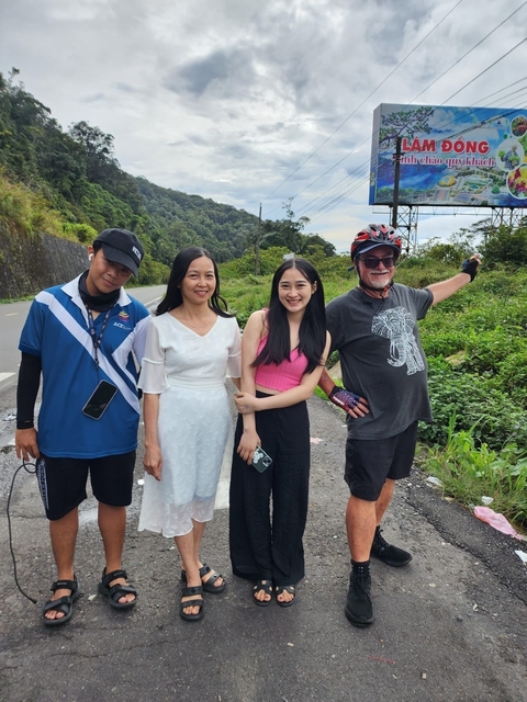       Four people posing by the roadside with vegetation in the background.
  