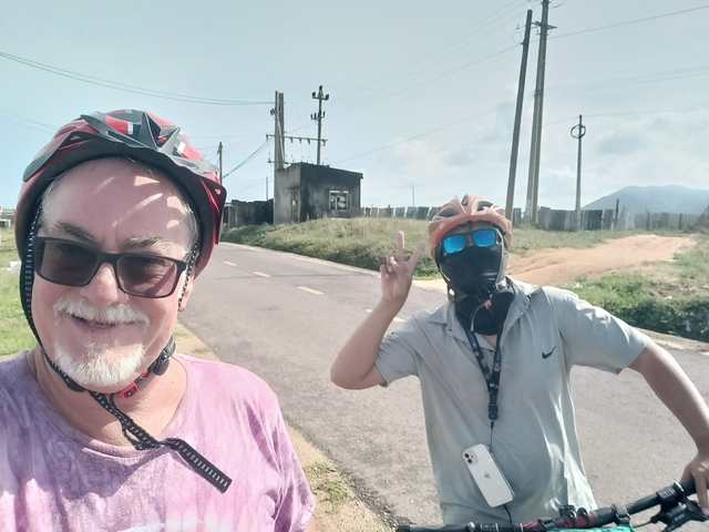       Two cyclists posing on a road with hills in the distance.
  