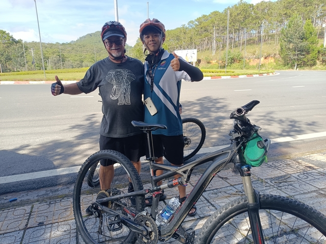       Cyclists posing with bikes on a scenic roadside.
  