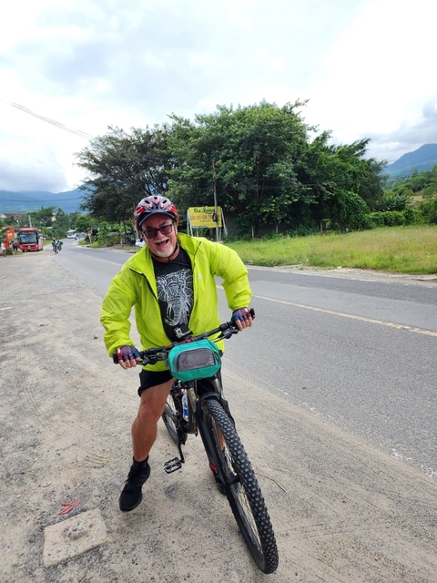       Smiling cyclist on a road surrounded by greenery.
  