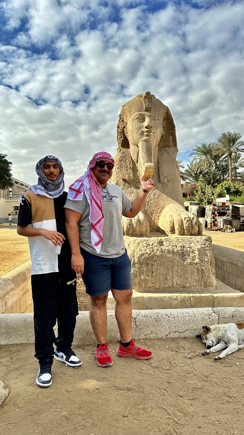       Two people posing in front of an ancient Egyptian statue.
  