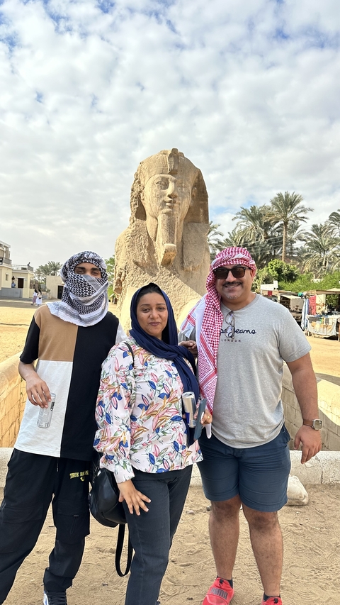       Three people posing in front of an ancient Egyptian statue.
  