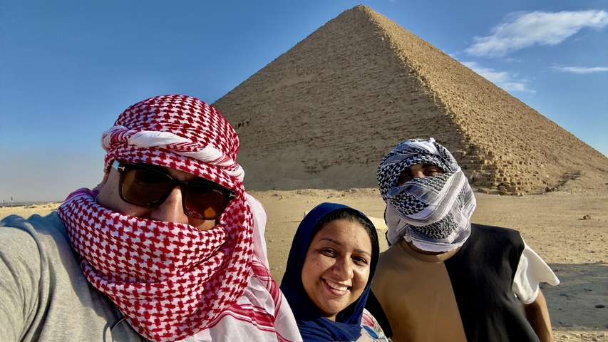       Three people posing in front of a pyramid.
  