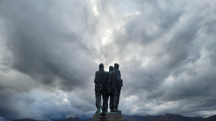 Statue of soldiers under a dramatic cloudy sky.