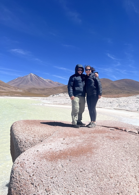       Couple standing beside a salt flat with mountains in the background.
  